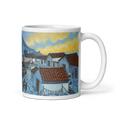Cargar la imagen en la vista de la galería, White mug featuring a painted coastal village with blue houses and red tile roofs at sunset
