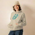 Bild in Galerie-Betrachter laden, Smiling person in desert dust unisex eco hoodie with teal graphic, beanie, and jeans